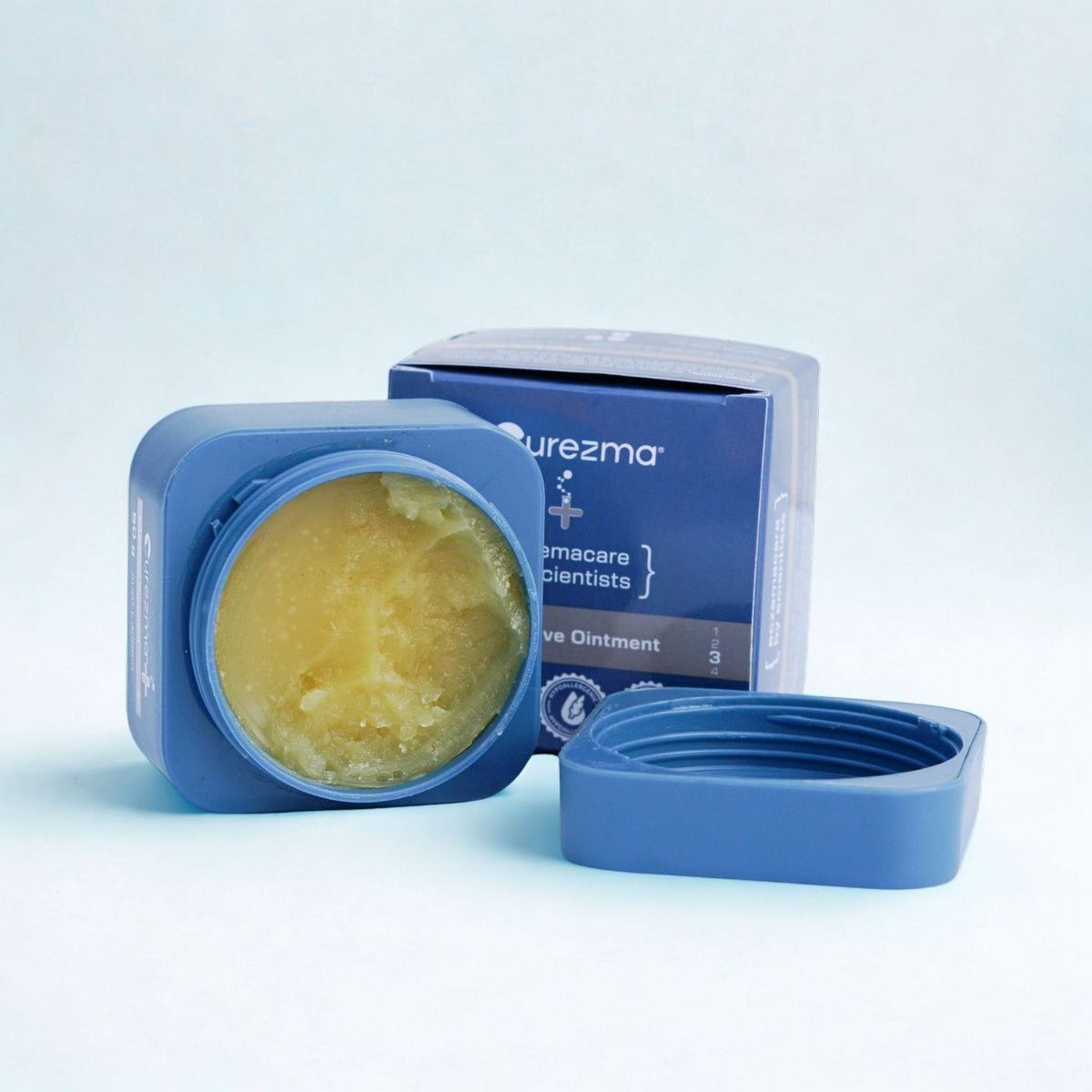 Blue container of ointment with lid removed on a light blue background